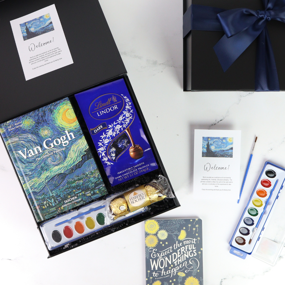 Gifting set with Van Gogh book, Lindt chocolate, watercolor set, and cards on a white surface.