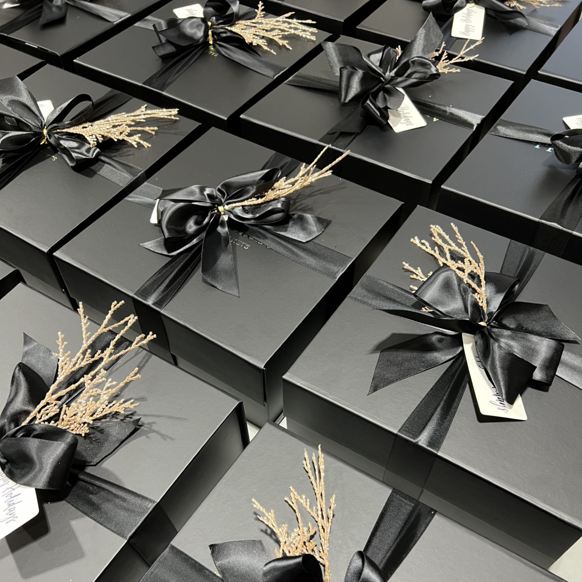Black gift boxes with black ribbons and gold accents arranged in a grid pattern.