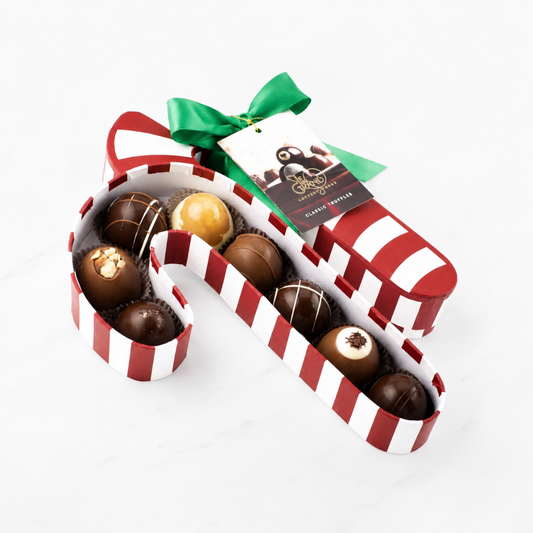 A  box of assorted chocolates arranged in a red and white striped candy cane shape, tied with a green ribbon and a chocolate tag, on a white marble background.