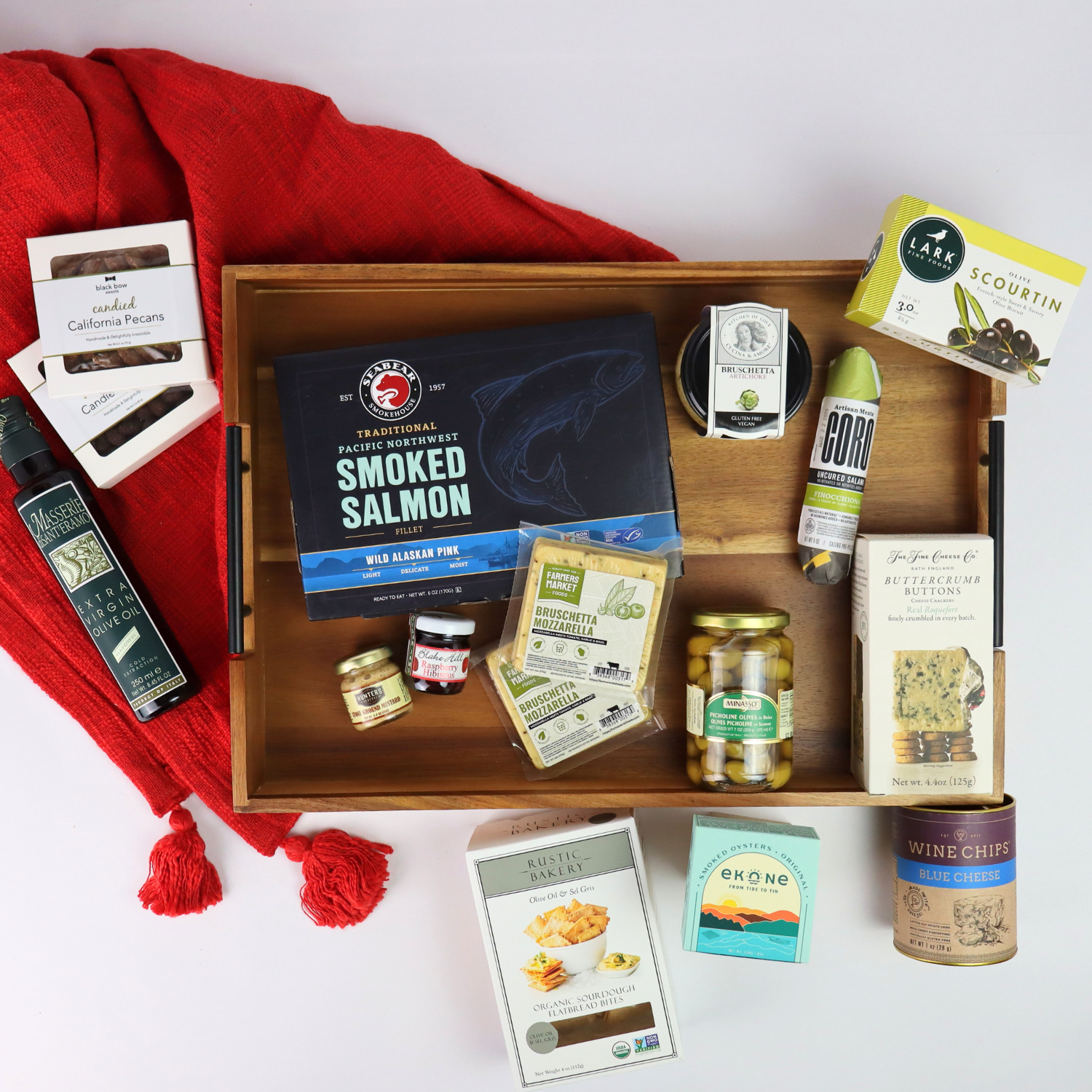 Festive holiday snack gift tray with smoked salmon, crackers, chocolates, and gourmet treats displayed with red holiday decor.