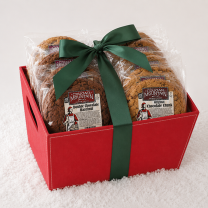 A red gift box filled with packaged chocolate chip cookies from Cougar Mountain, set on a white textured surface with a green ribbon.