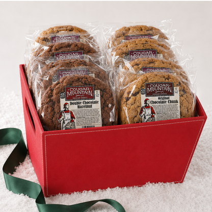 A red gift box filled with packaged chocolate chip cookies from Cougar Mountain, set on a white textured surface with a green ribbon.