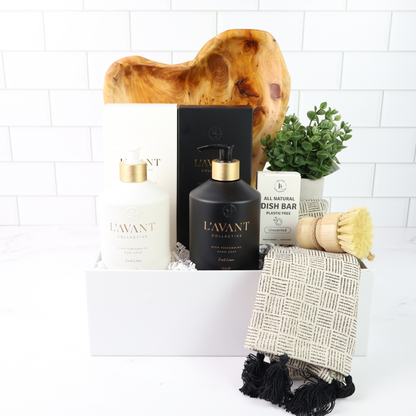 Collection of L'AVANT products including a bottle, candle, and soap on a white surface with a wooden block and plant in the background.