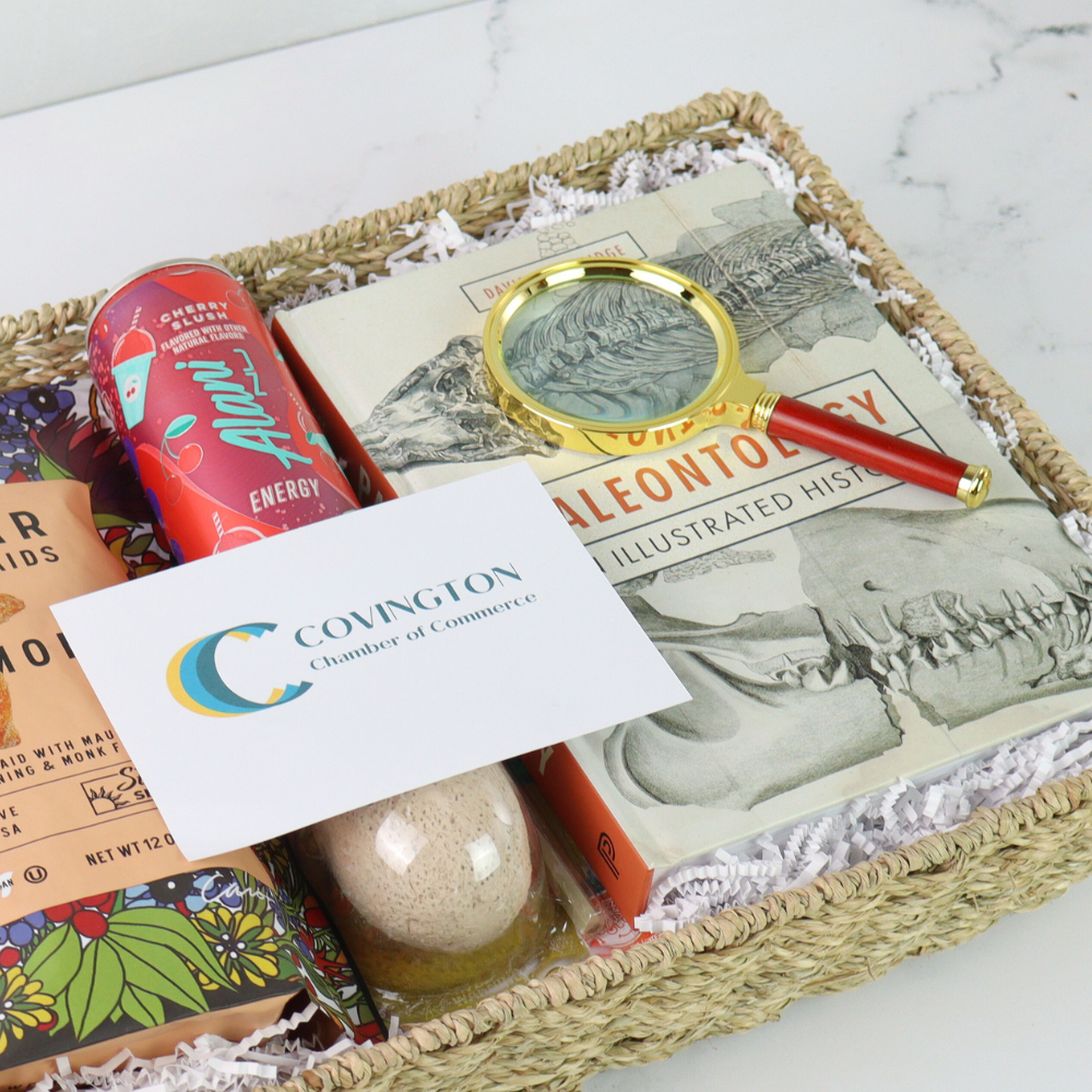 Basket with books, a magnifying glass, and a card with 'Covington' logo on a white surface.