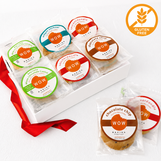 A white gift box containing several individually wrapped chocolate chip cookies, each with a round colorful label. One cookie package is placed in front of the box, and another package is partially visible behind it.
