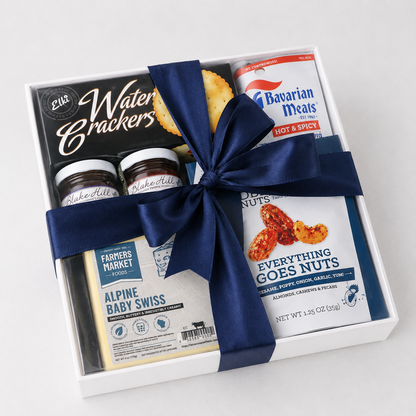 A gourmet gift hamper box containing a water cracker snack, two jars of Raskimoff's Alpine Baby Swiss cheese, a bag of Bavarian Meats hot and spicy sausage, and a package of Everything Goes Nuts, tied together with a navy blue satin ribbon.