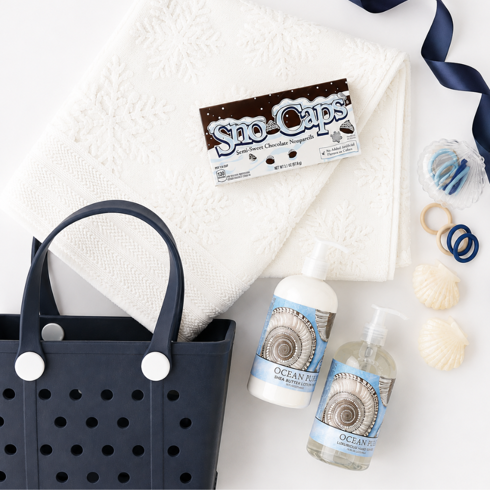 A curated gift set featuring a navy blue perforated tote bag, a white textured towel, two bottles of Ocean Caps hand wash and shampoo, a bar of Sao-Caps chocolate soap, and seashells on a white background.