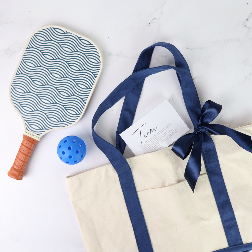 Paddle ball racket with blue pattern, small blue ball, and gift bag with blue ribbon on a white background