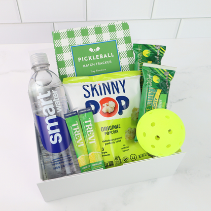 Pickleball-themed gift box with Skinny Pop popcorn, smartwater bottle, and pickleball equipment on a white background