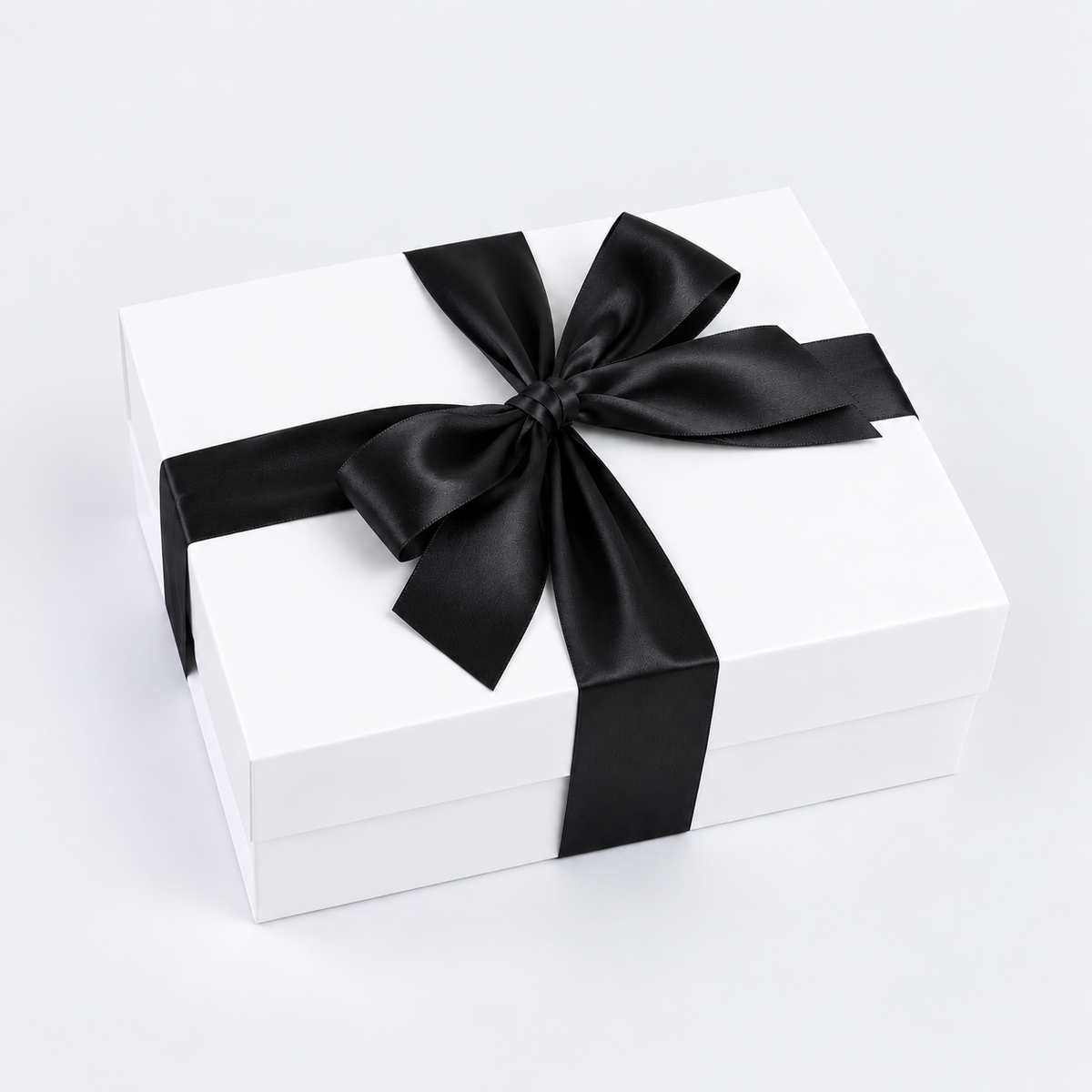 A white rectangular gift box tied with a wide black satin ribbon and bow, photographed on a clean white studio background.