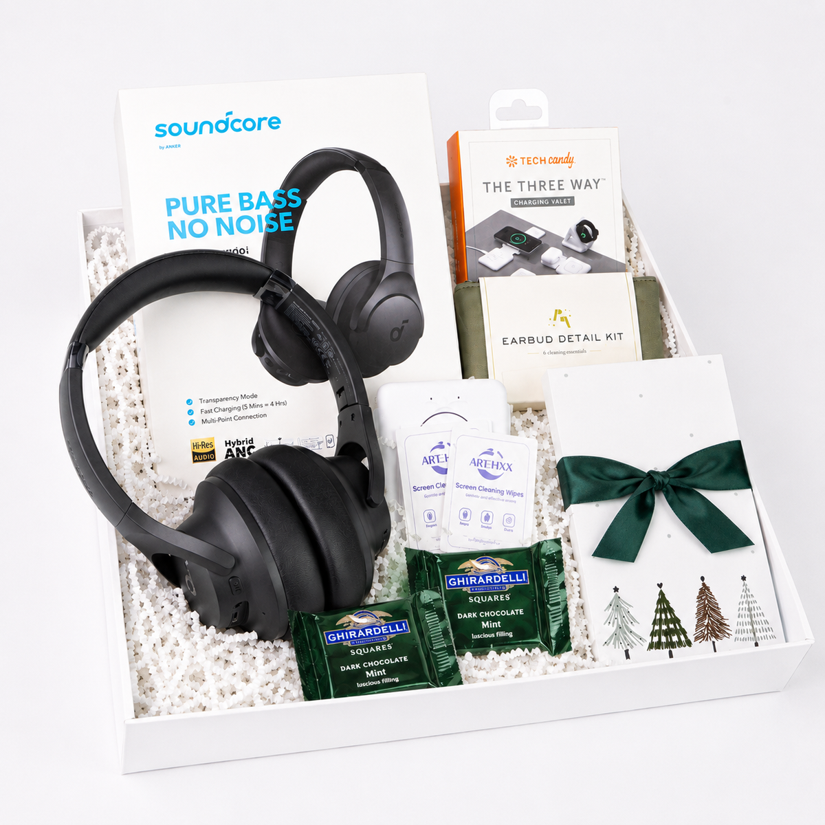A curated gift box set containing a pair of black Soundcare over-ear headphones, a Soundcore Pure Bass No Noise card, a Nintendo earbud detail kit box, a packet of Ghirardelli chocolate, and a white card tied with a dark green ribbon.