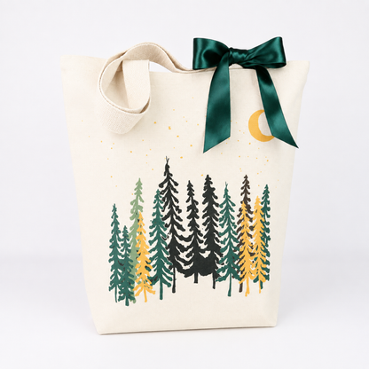 An off-white canvas tote bag with a dark green satin bow and a forest tree print in green, black, and yellow, set against a plain white background.