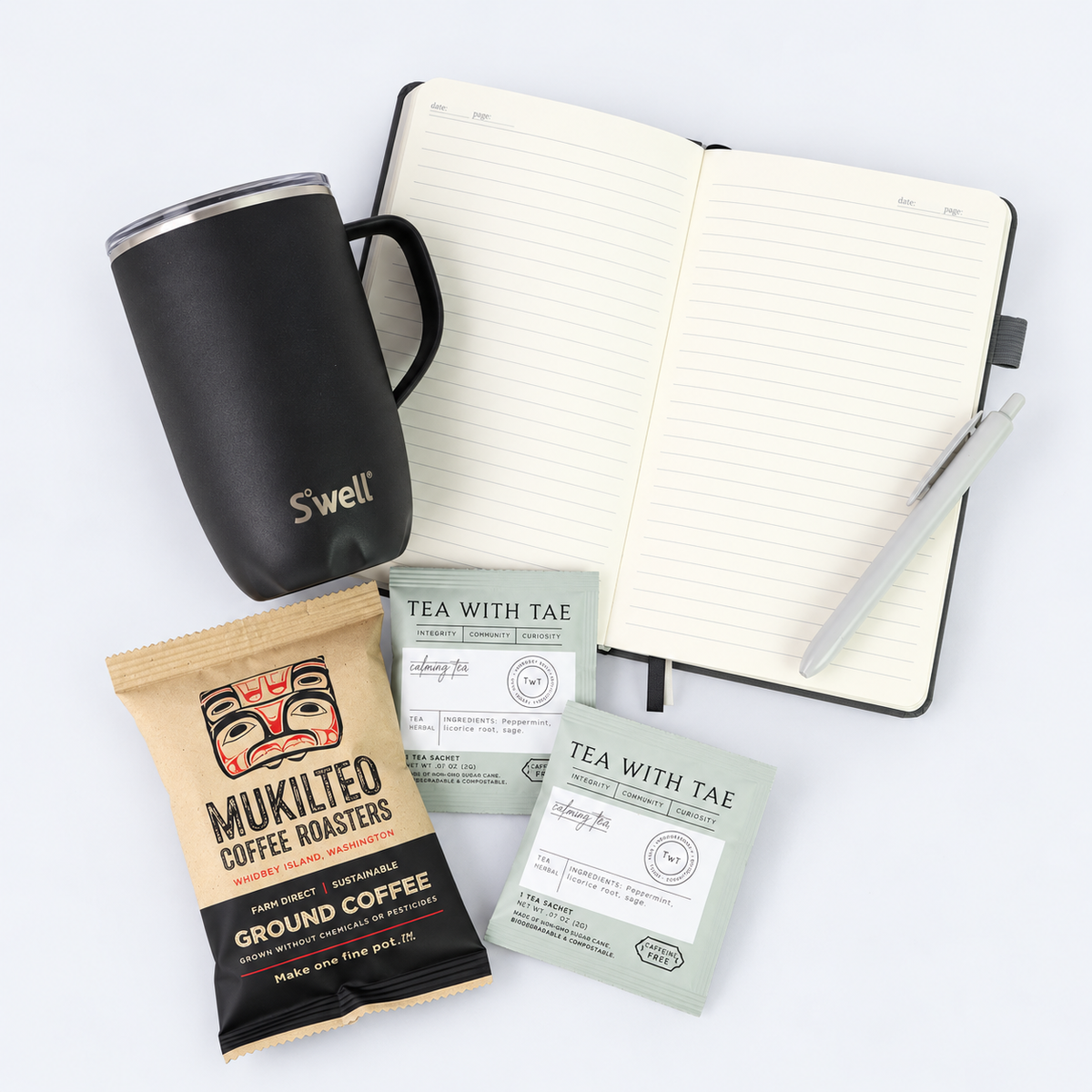 Overhead view of coffee gift set featuring black S'well tumbler, open gray notebook with pen, Washington-roasted coffee and two herbal tea sachets.