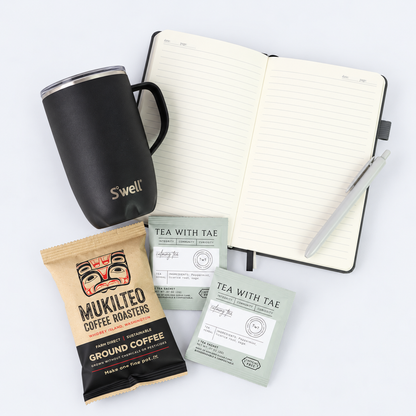 Overhead view of coffee gift set featuring black S'well tumbler, open gray notebook with pen, Washington-roasted coffee and two herbal tea sachets.
